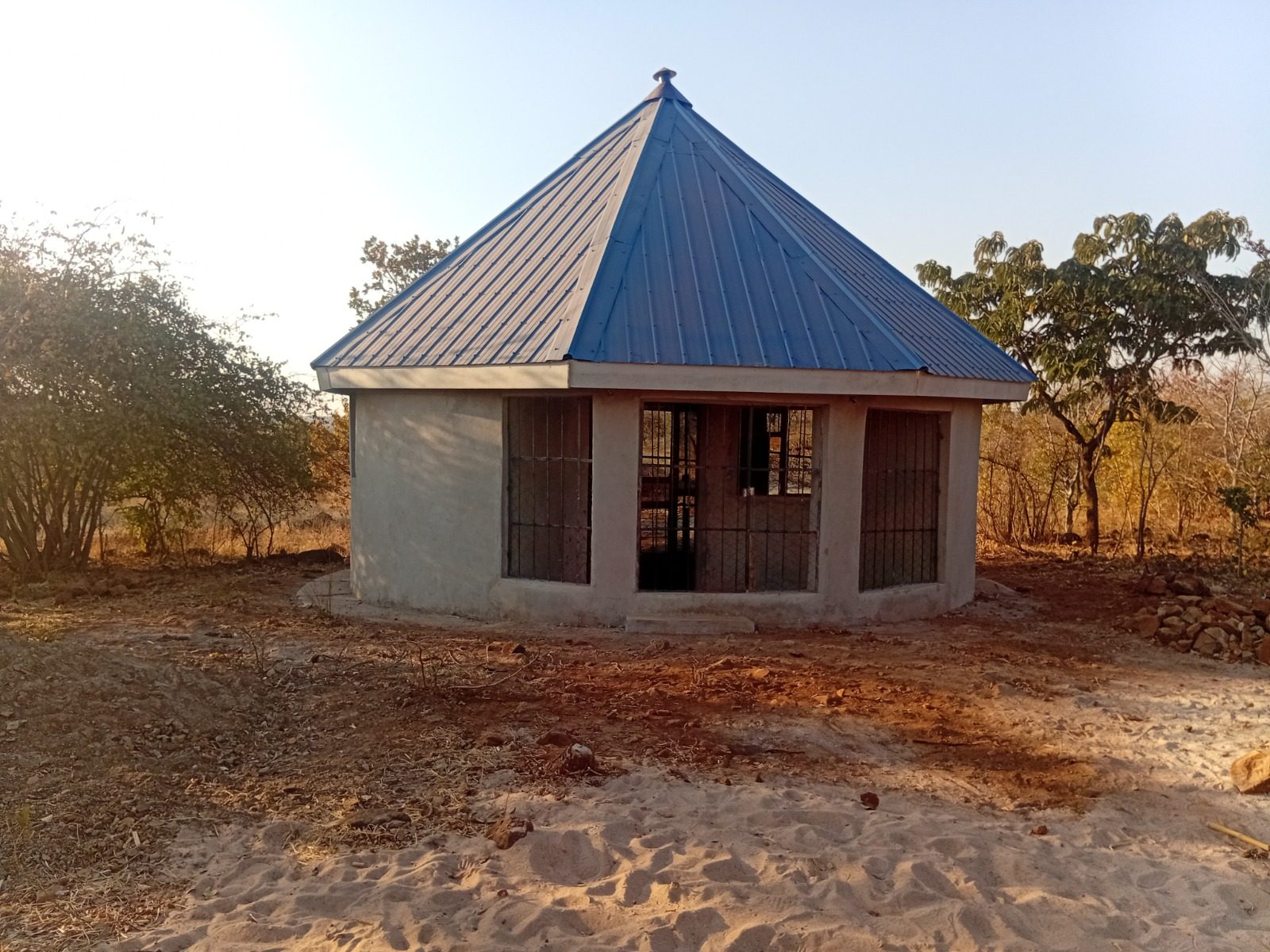 Round plastered building with a blue metal roof and barred openings