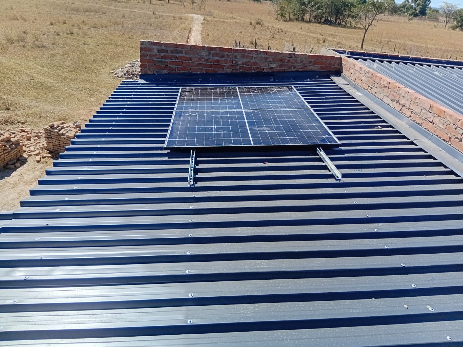 Solar panel mounted on a dark metal roof with grassland beyond
