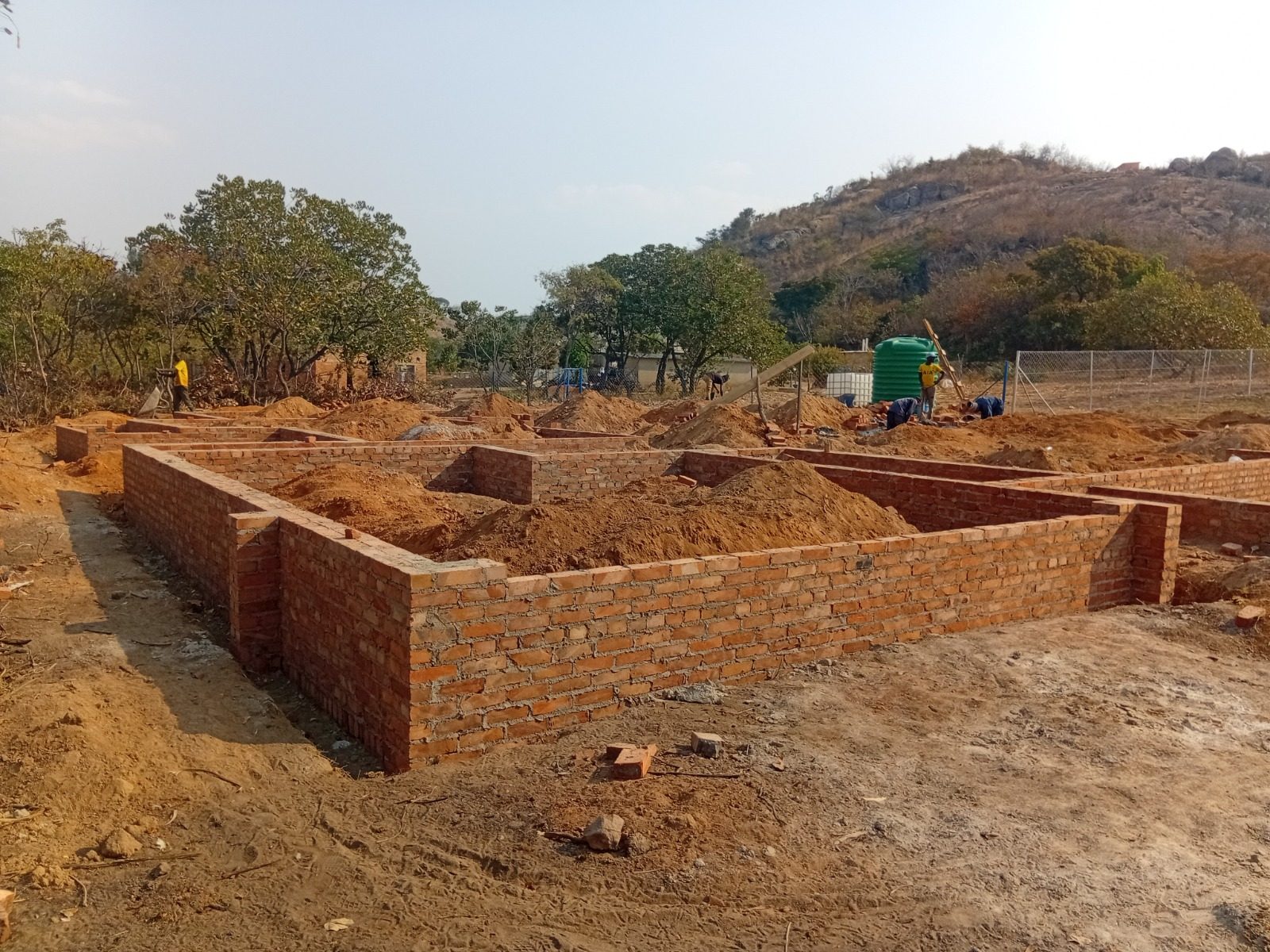 Brick foundation walls on a red-soil site with hills behind